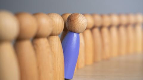 An image of a wooden peg person leaning out from a line of other peg people.