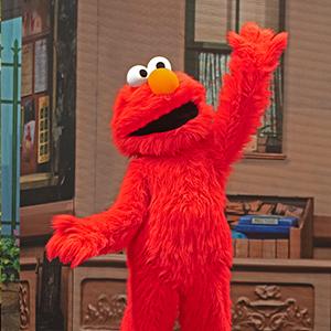 Elmo standing and waving on Sesame Street.