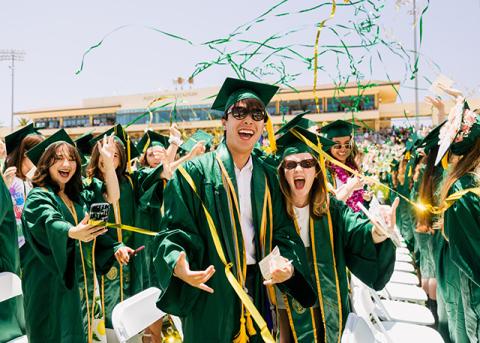 Cal Poly graduates celebrating during commencement as green and gold streamers fly overhead.