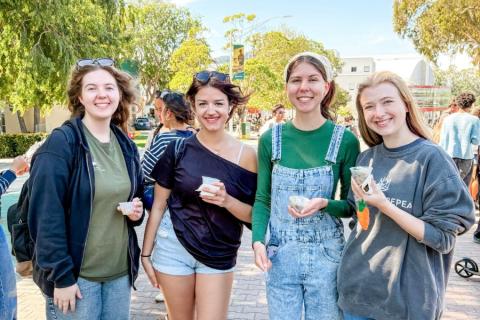 Attendees sample food on Mustang Way, with campus walkways and event activity visible in the background.