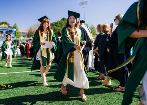 Cal Poly graduates in caps and gowns walk across the field during commencement.