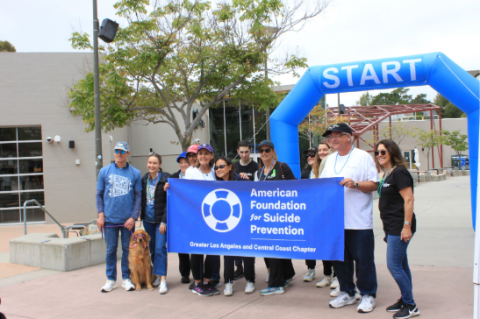 Participants of a previous AFSP Out of the Darkness Walk holding a sign in front of the start area.