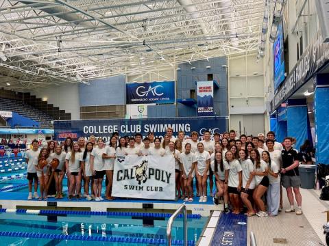 The Cal Poly Swim Club standing by the pool with a school banner.