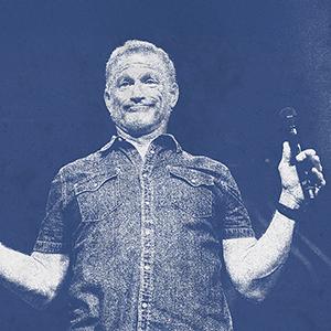 Tim Hawkins on stage holding a microphone.