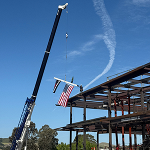 A construction crew using a crane to top out a new facility with an American flag.