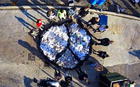 A group of people standing around a giant peace sign made of garbage.