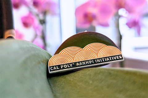 Cal Poly branded AANHPI Initiatives Lapel Pin sitting on an orchid flower.