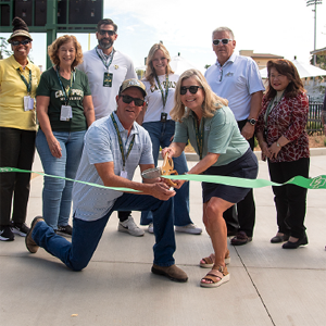 Andrea Burns cutting a ribbon with another person and a group of people behind them.