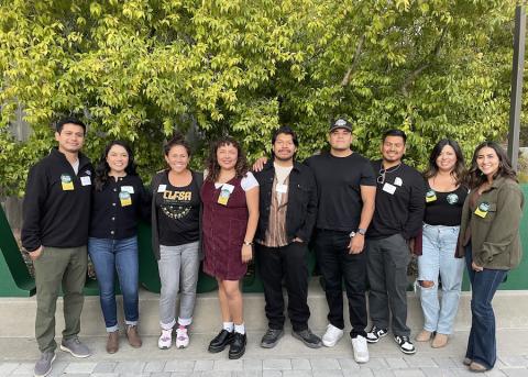 A group of Cal Poly alumni and members of the Cal Poly Chicanx/Latinx Faculty Staff Association smile while standing outdoors in front of trees.