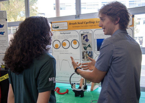 Two students standing in front of a display board and discussing a project.