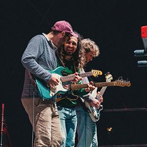 Members of Próxima Parada playing guitars on stage.
