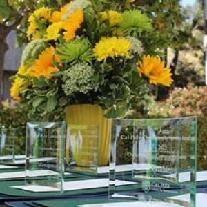 A table with Learn by Doing Good Awards and a vase full of flowers on it.
