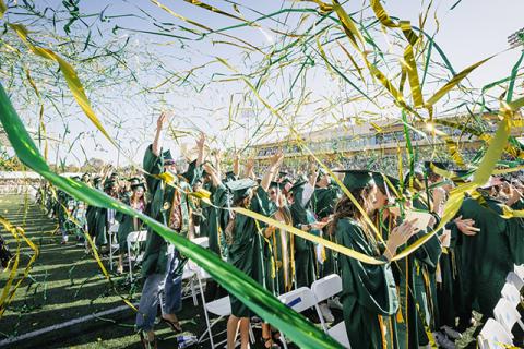 Cal Poly graduates celebrate during commencement as green and gold streamers fly overhead.