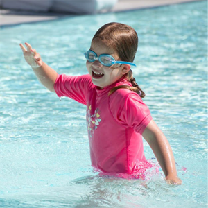 A little girl in the pool wearing a pink swim shirt and goggles.