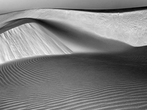 A black-and-white photograph of the Oceano Dunes, showing sweeping sand dunes devoid of people and vegetation.