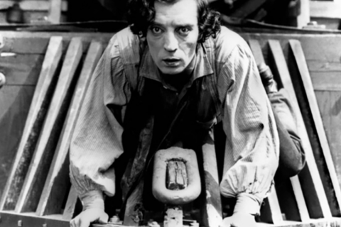 Movie still from “The General” of Buster Keaton on the front of a train engine.