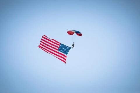 A parachuter floating through the sky with an American flag hanging from their leg.