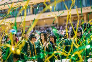 Happy graduates clap as streamers rain down around them.