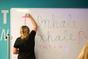 A student writes 'Inhale, Exhale' on a whiteboard inside the pop-up resilience room.