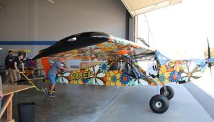 A professor and student push a floral-patterned Rans S-21 Outbound aircraft named Velma into the sunlight at the San Luis Obispo Airport.