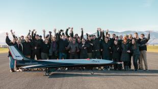 A group of people standing on a runway cheer in front of a small spaceplane.