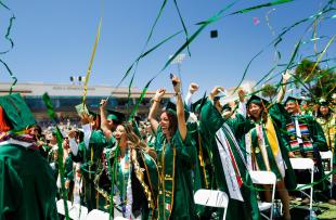 Graduates in the College of Engineering cheer at their commencement ceremony as green and gold streamers rain down.