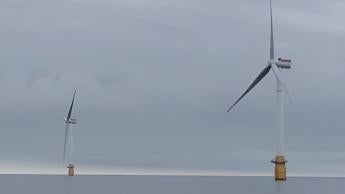 Two wind turbines rise from the surface of the ocean in front of an overcast sky