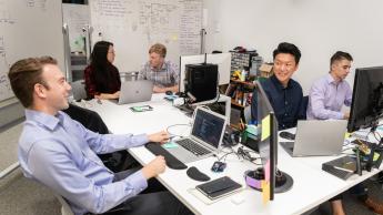 Five students sit at desks in the Hot House facing computers and hardware
