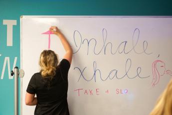 A student writes 'Inhale, Exhale' on a whiteboard inside the pop-up resilience room.