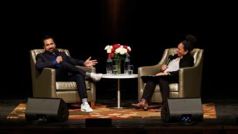 Actor Kal Penn smiles from the stage as he sits in an armchair across from professor Denise Isom. 