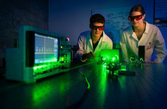 Two students observe a laser while wearing protective gear.