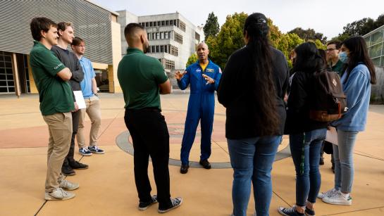 Astronaut Victor Glover wears a blue flight suit while talking with students in the Engineering Plaza at Cal Poly