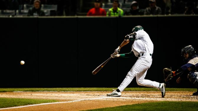 A baseball player swings the bat as the pitch approaches
