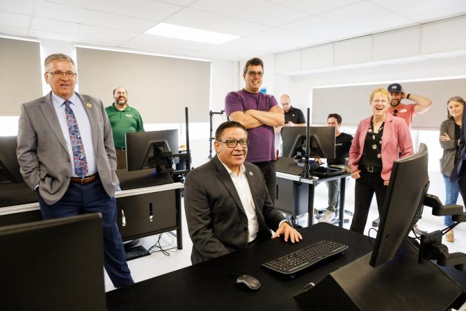 Congressman Salud Carbajal, center, sits at a desk with a computer in front of him while Cal Poly President Jeffrey Armstrong, Engineering Dean Amy Fleischer, Professor Paul Iscold and other people stand behind him.