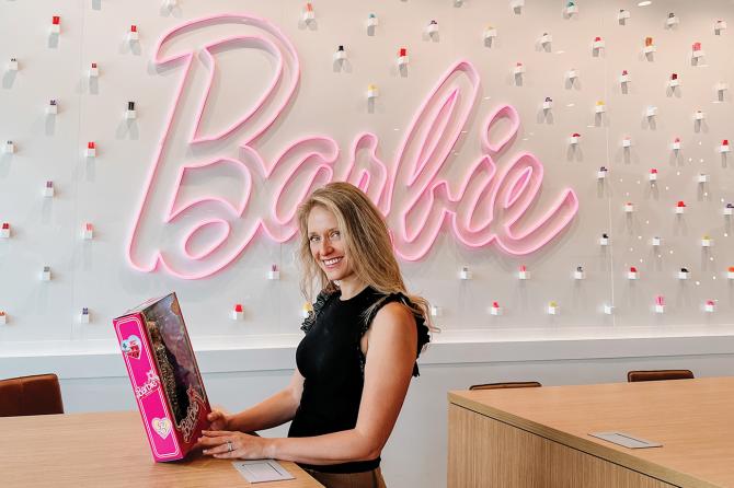 Alumna Krista Berger stands in front of a neon Barbie sign