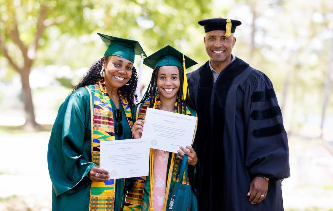 From left: Dionna Glover, Genesis Glover and Victor Glover, all wearing graduation regalia, smile for a family photo. Dionna and Genesis both hold their diplomas.