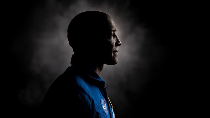 Astronaut Victor Glover stands in profile in a blue flight suit