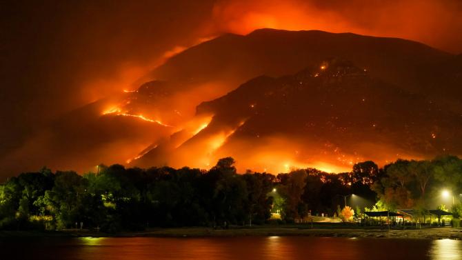 A wildfire glows in the hills above an urban area at night