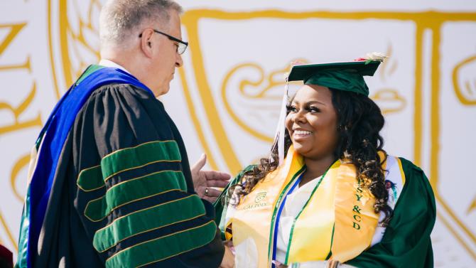A university president shakes hands with a student in regalia at a commencement event