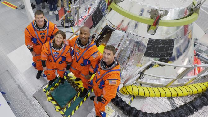 Four NASA Astronauts in orage space suits stand next to the Orion capusule