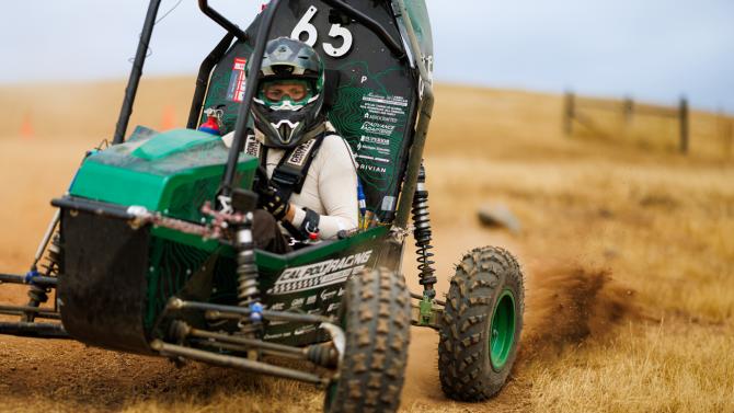 A driver at the wheel of an off-road Baja vehicle on a dirt track