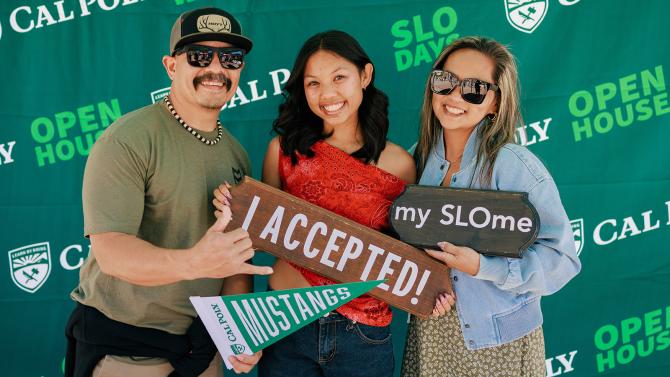 An accepted student and her family holding signs in front of a Cal Poly backdrop.