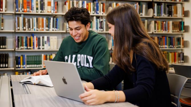 Two students looking at a laptop screen in the library.