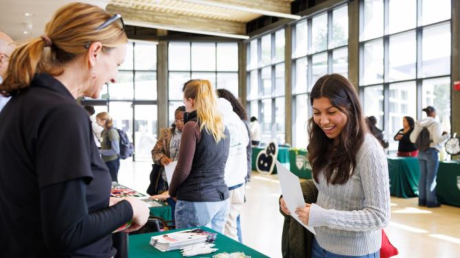 A prospective student talking to a Cal Poly representative at an informational booth during a college fair.