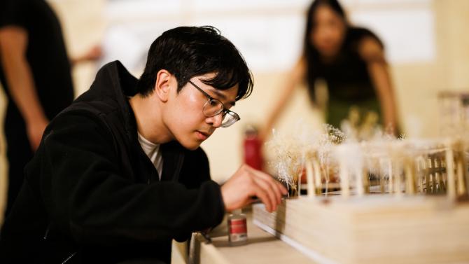 A student adds small trees around a model of a structure design