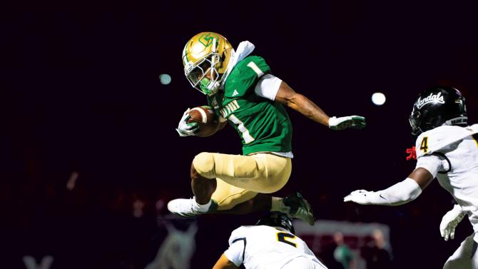 A Cal Poly Football player jumps over a defender while holding the football